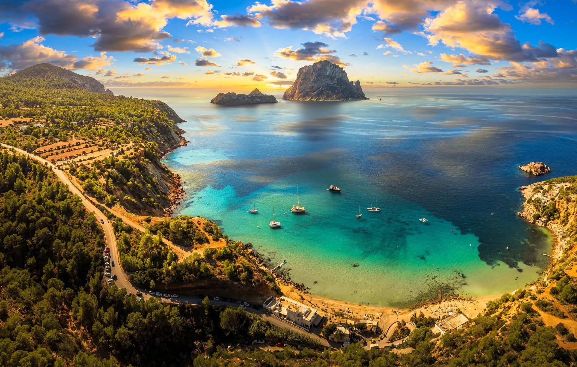 Aerial view of a tropical bay with turquoise water, sandy beaches, and rocky green hills under a cloudy sky