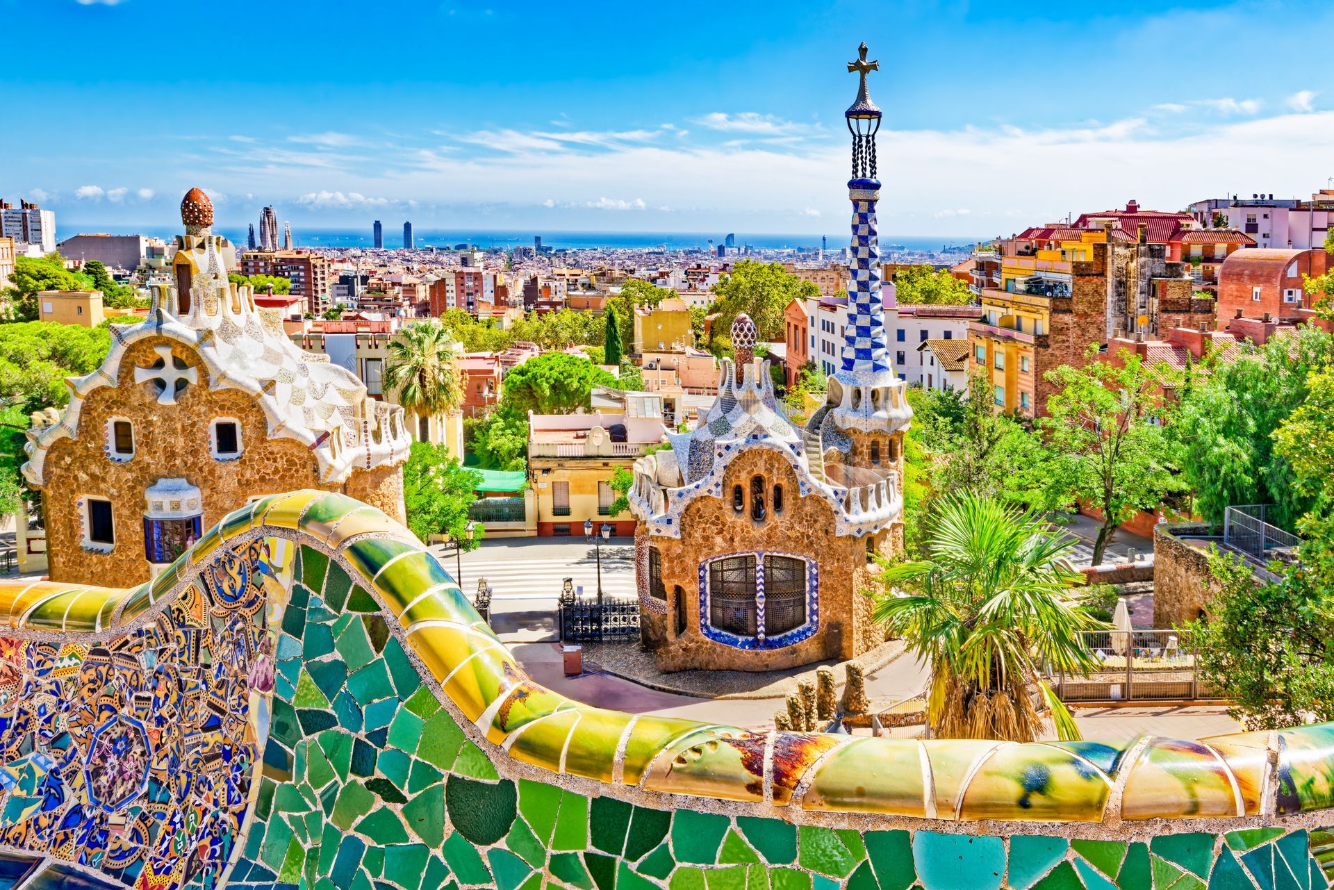 Colorful mosaic benches and towers in Park Güell overlooking Barcelona skyline on a sunny day