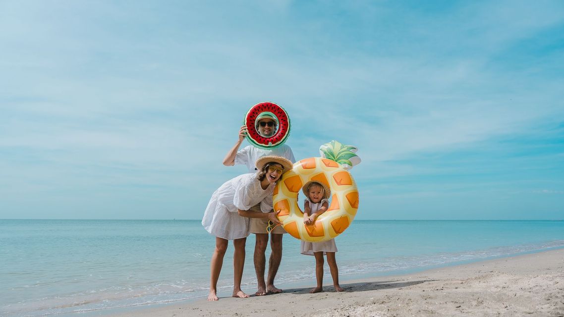 Three people posing on a beach with colorful swim rings under a blue sky
