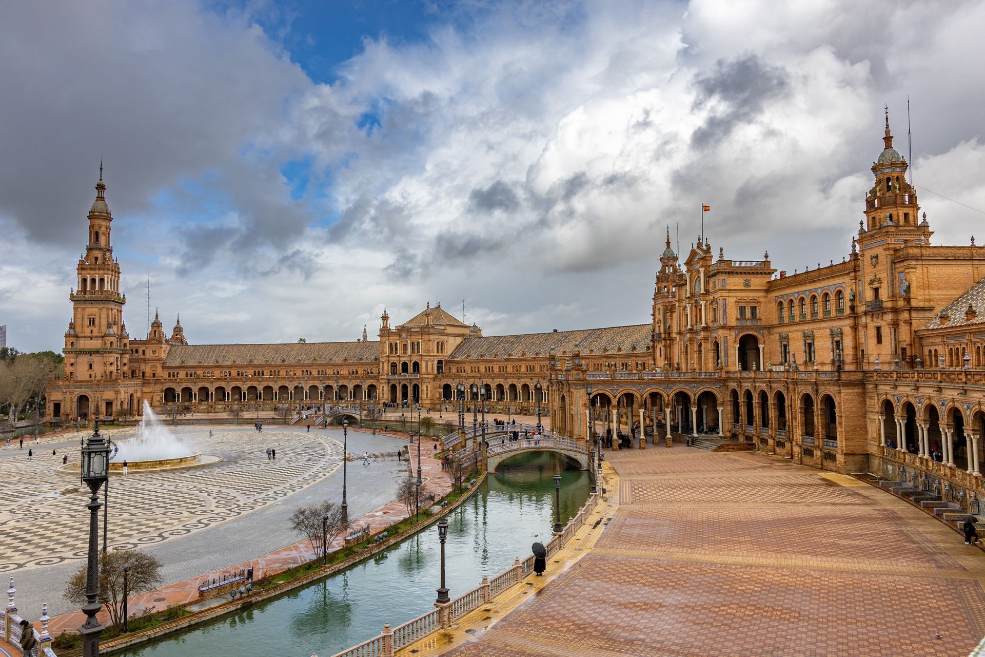 Plaza de España in Seville with ornate buildings, a canal, and a cloudy sky