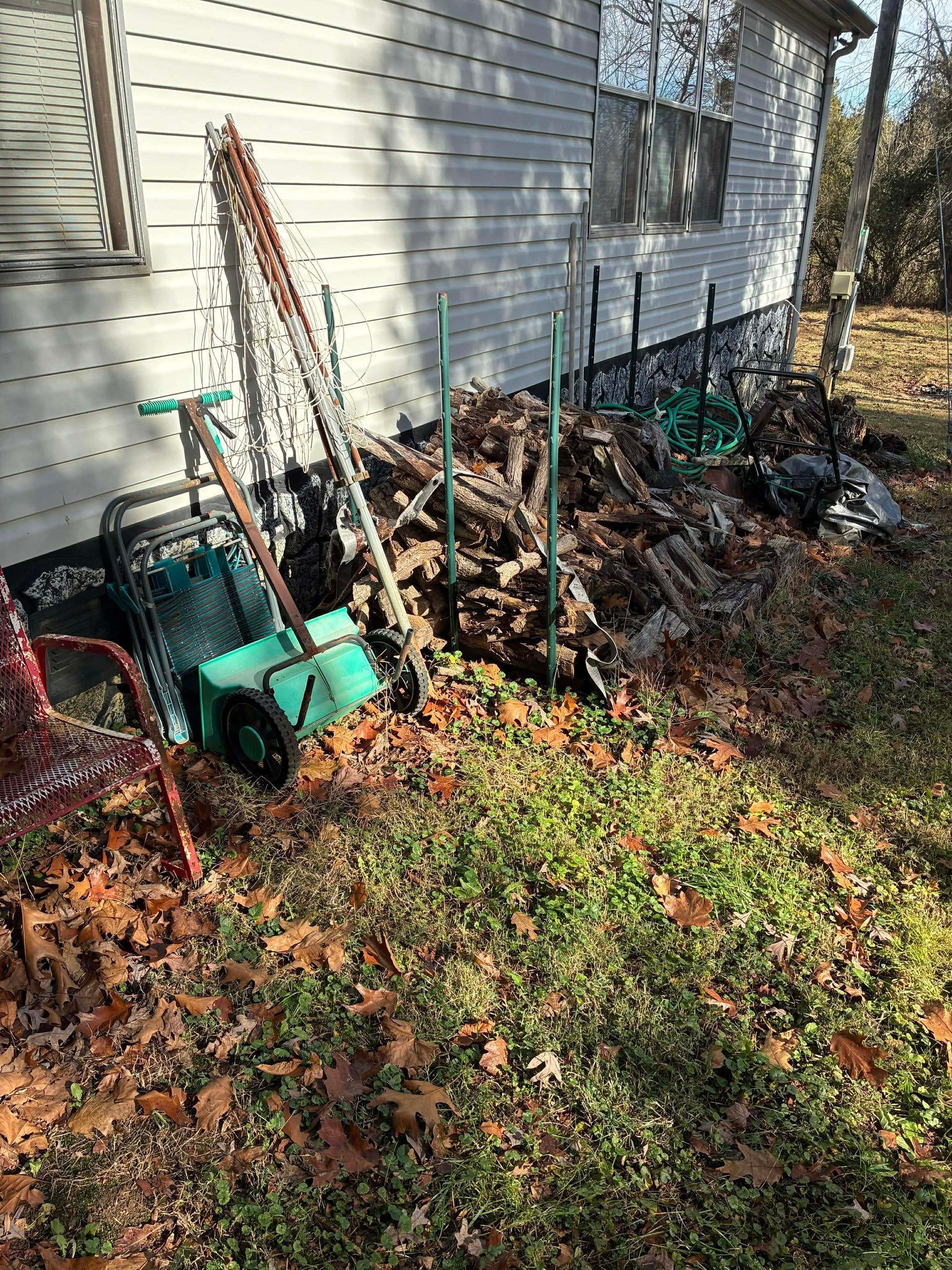 Gardening tools and stakes piled beside a house in a leaf-covered yard