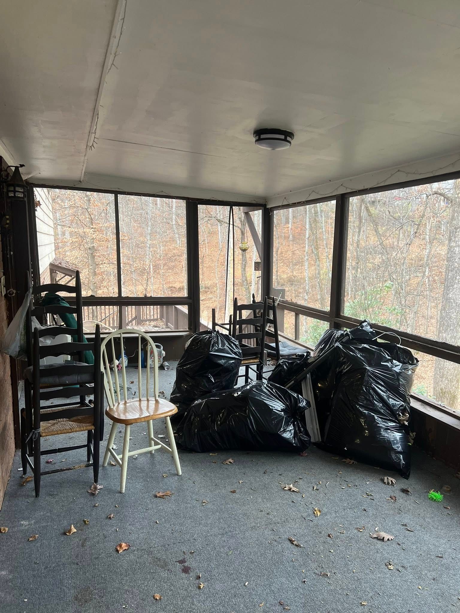 Screened porch with stacked chairs, a white chair, and black bags on carpeted floor.