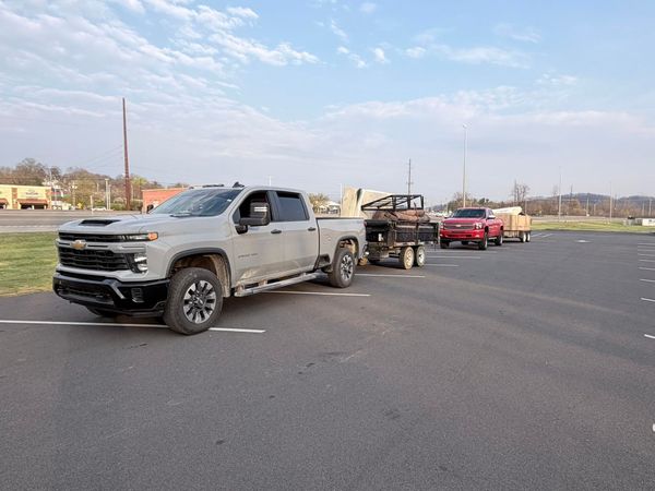 Silver pickup truck towing a trailer with a red car on an open parking lot