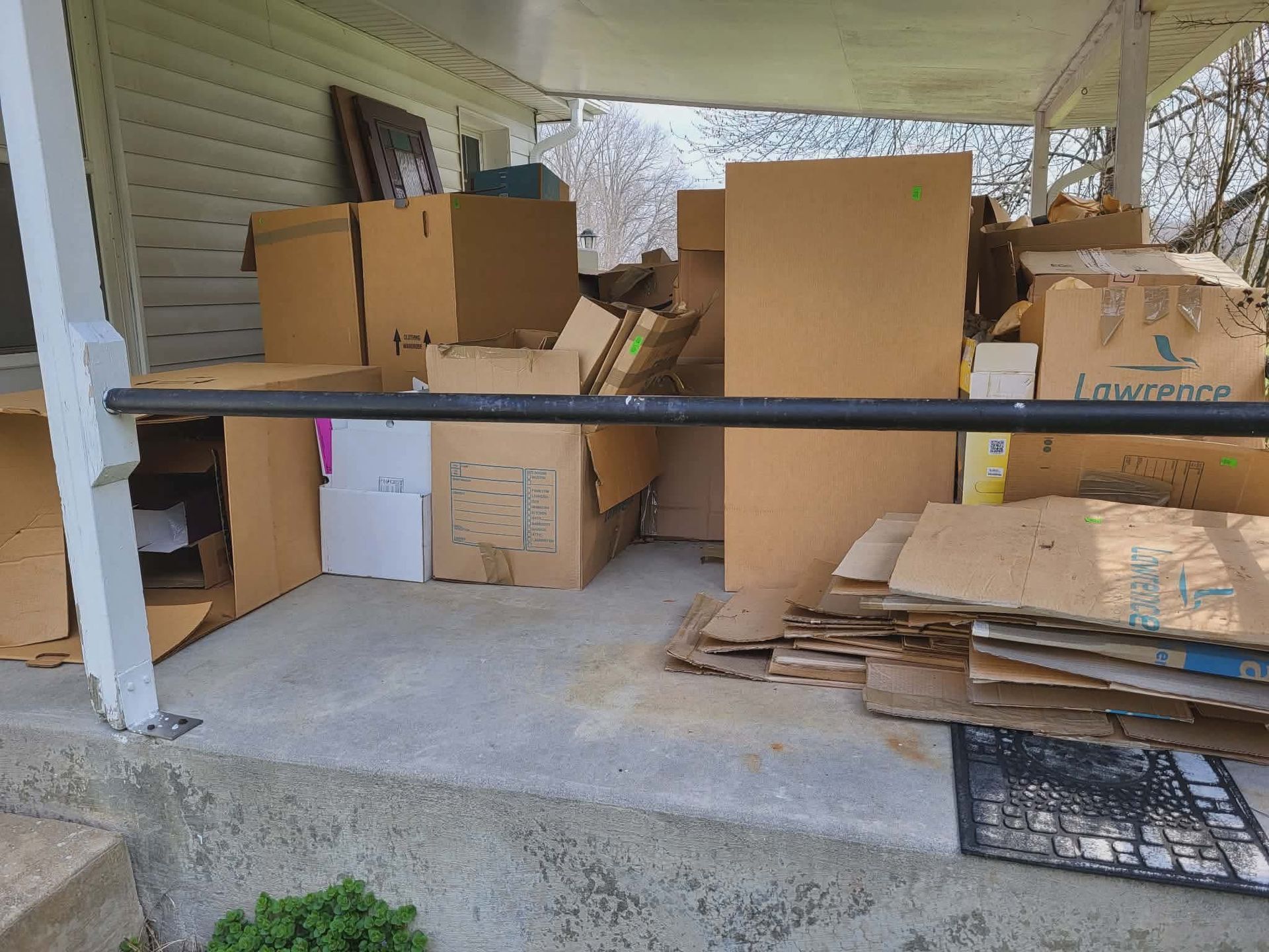Porch cluttered with stacked cardboard boxes, flattened boxes, and a few small packages.