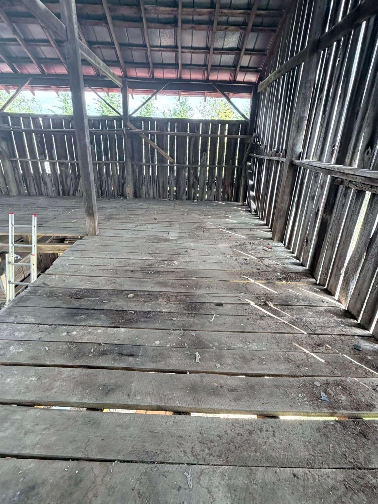 Empty rustic wooden shed with a weathered plank floor and slatted walls under a tin roof