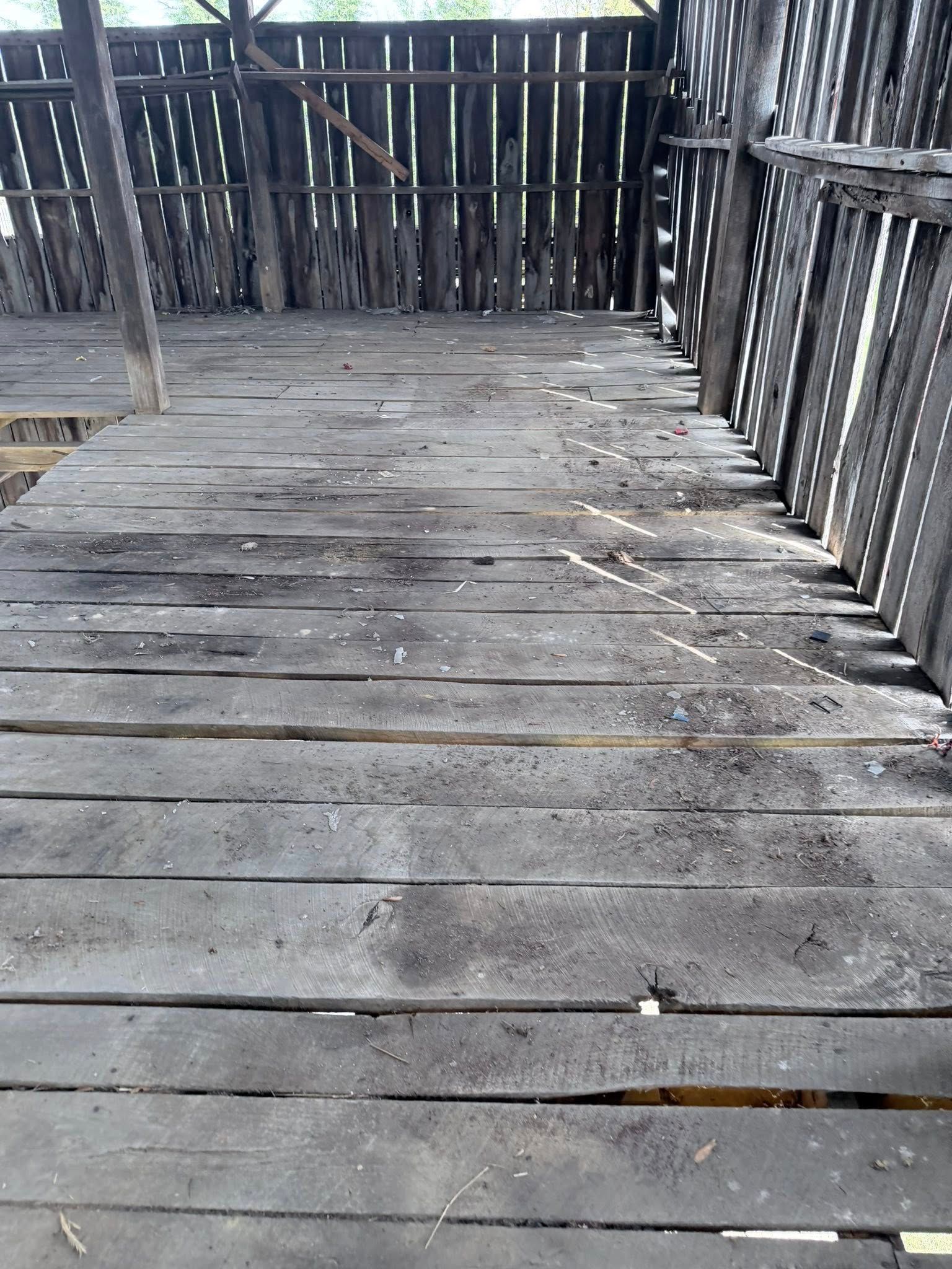 Weathered wooden deck with cracked planks and a railing, showing wear and damage.