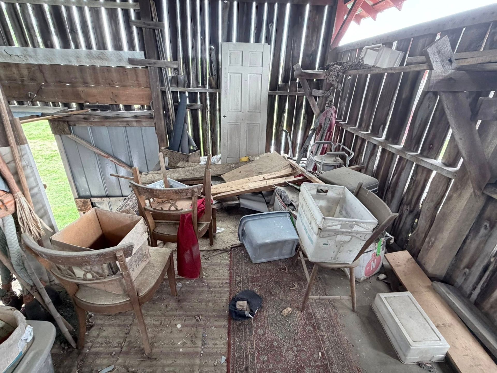 Damaged shed interior with broken furniture, scattered debris, and a red fire extinguisher on the floor.