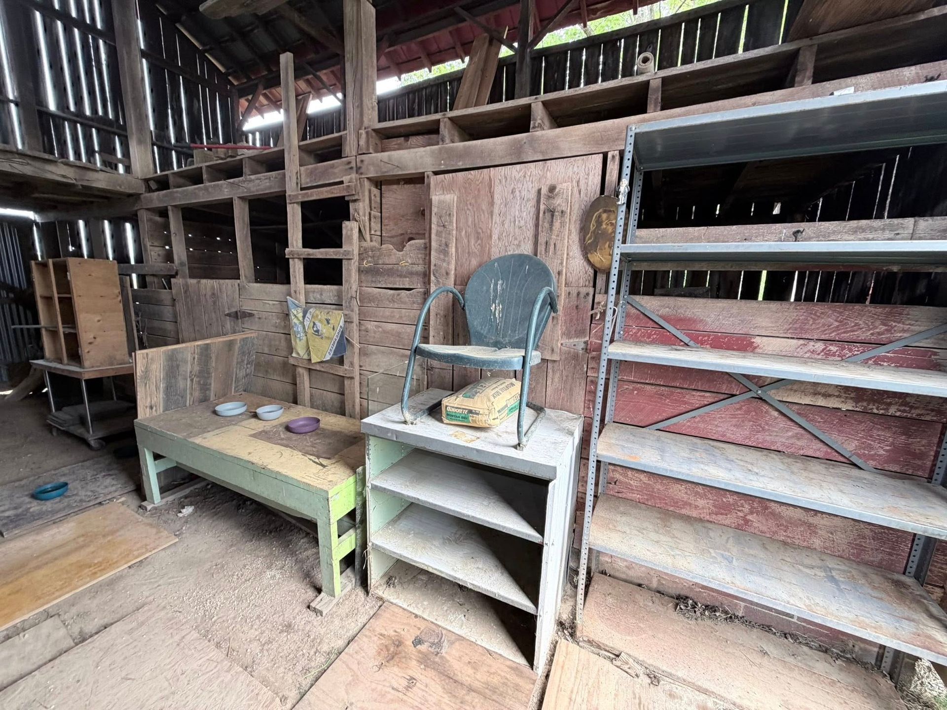 Rustic barn interior with old shelves, a chair, and a green bench on a wooden floor.