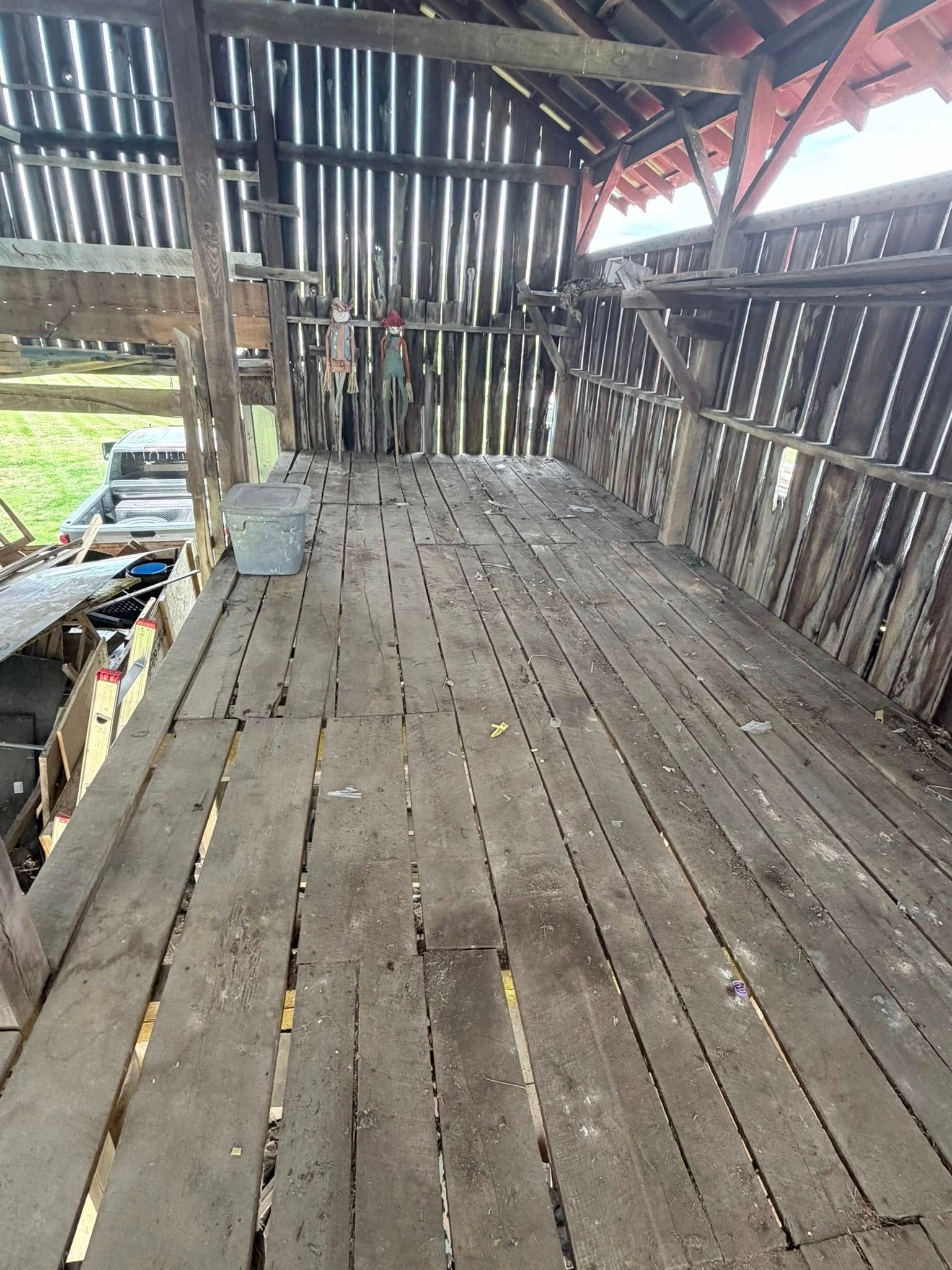 Weathered wooden barn interior with slatted walls and a rough plank floor, showing daylight through gaps.