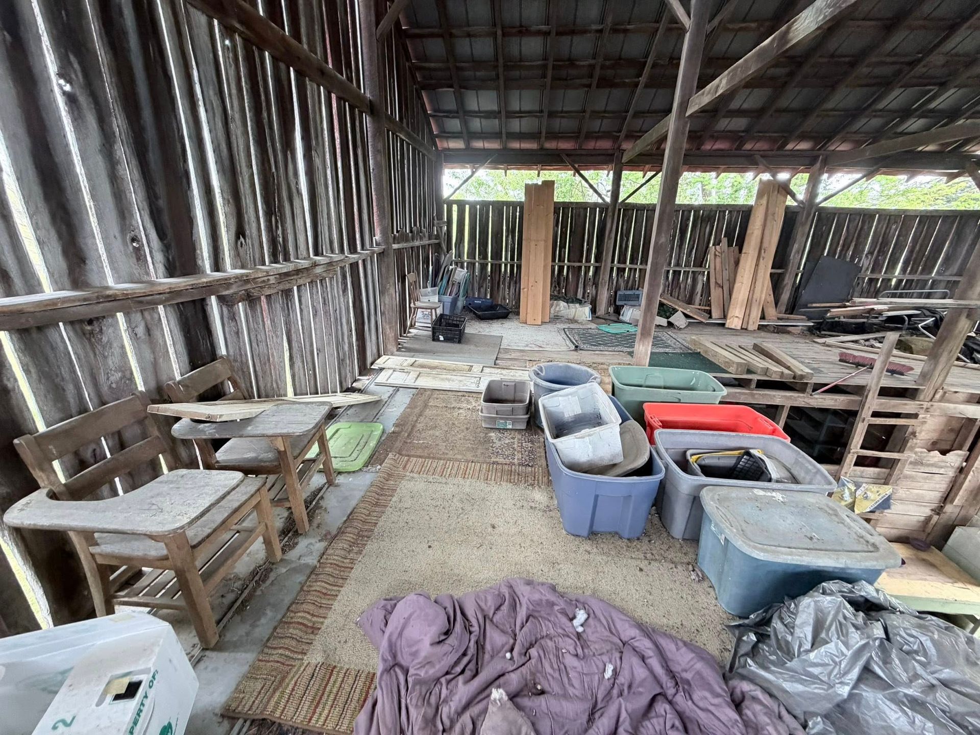 Rustic wooden shed interior with rows of buckets, stools, tables, and cloths on the floor