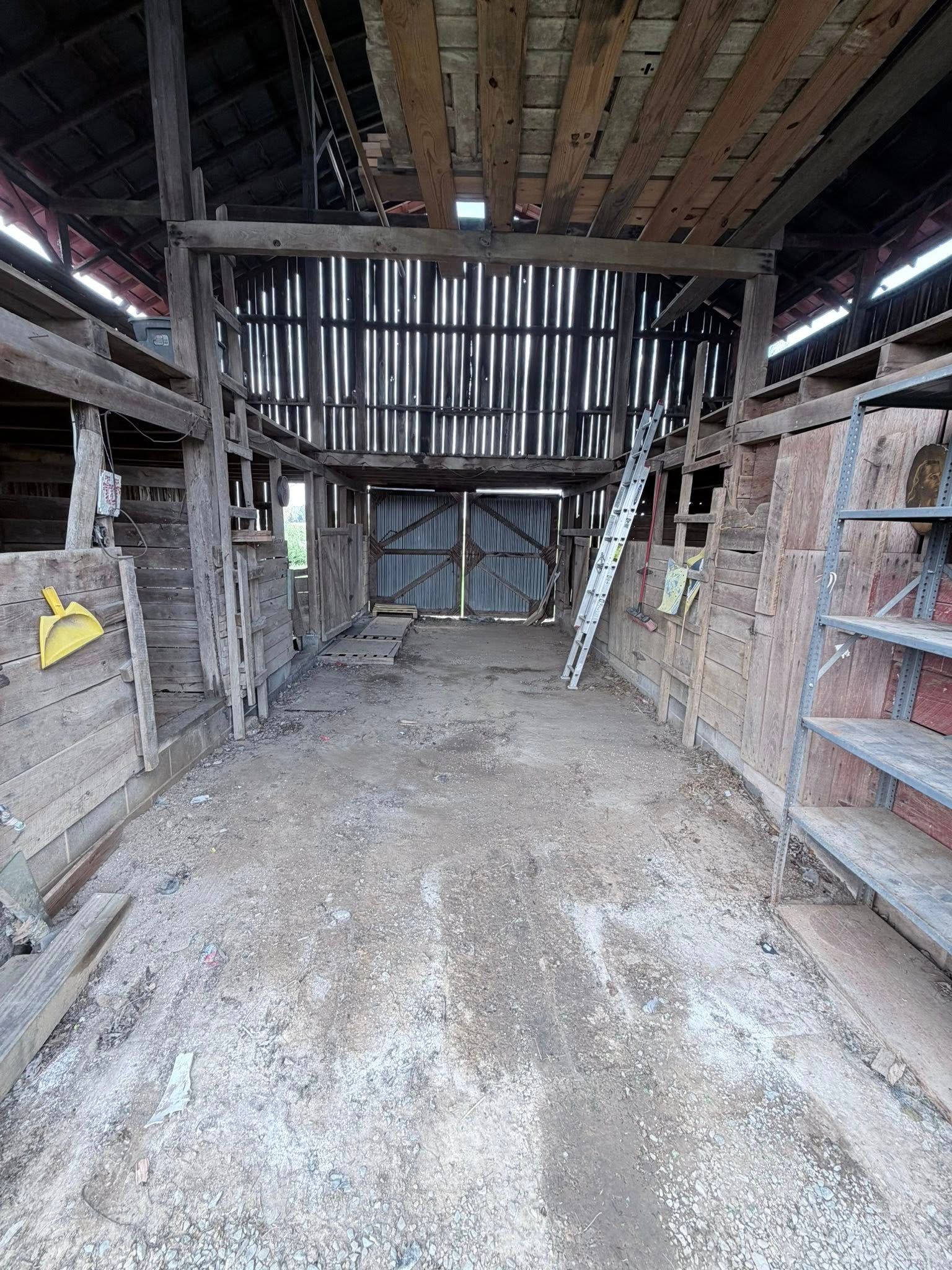 Inside a rustic barn, empty dirt floor, exposed beams, and brick walls with shelves on both sides.