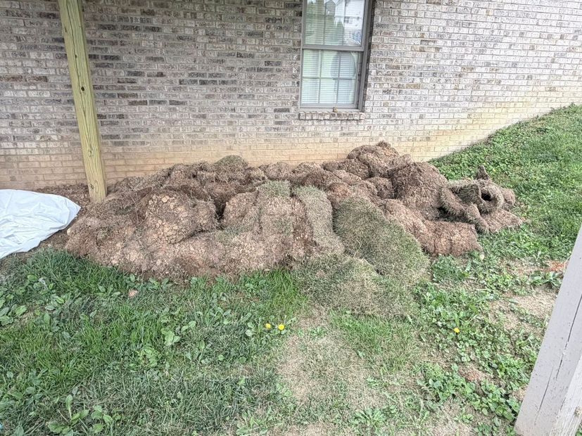 Large pile of dirt or mulch on grass beside a brick house under a window