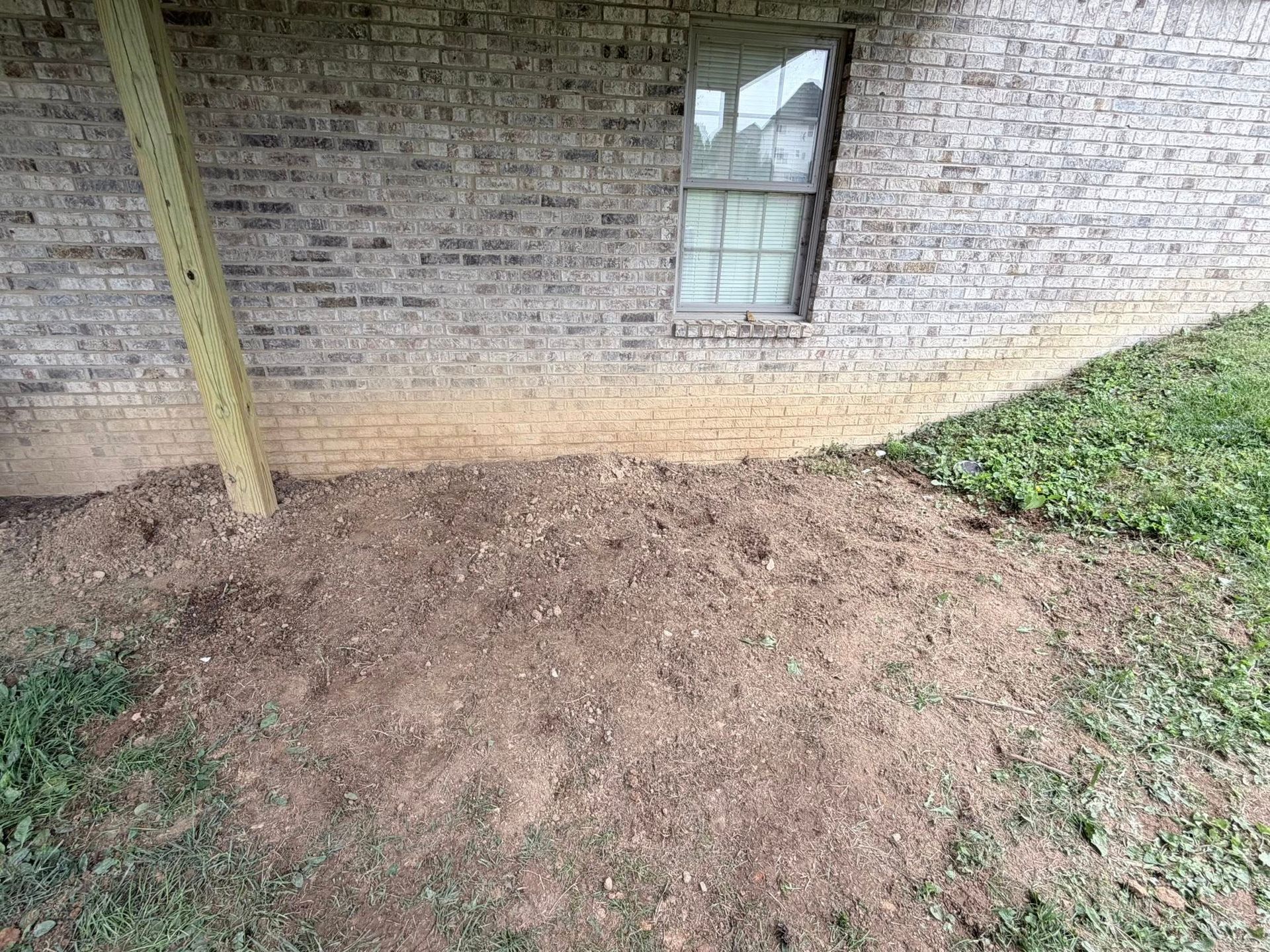 Fresh soil pile beside a brick house wall under a window and wooden post