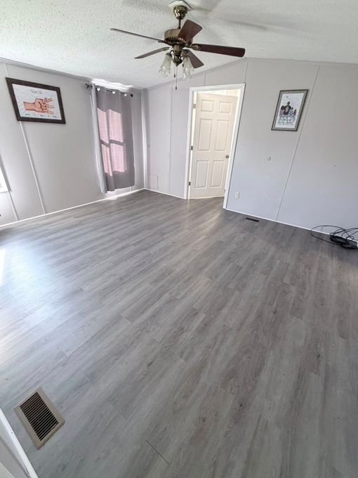 Empty bedroom with gray flooring, white walls, ceiling fan, and closet doors.