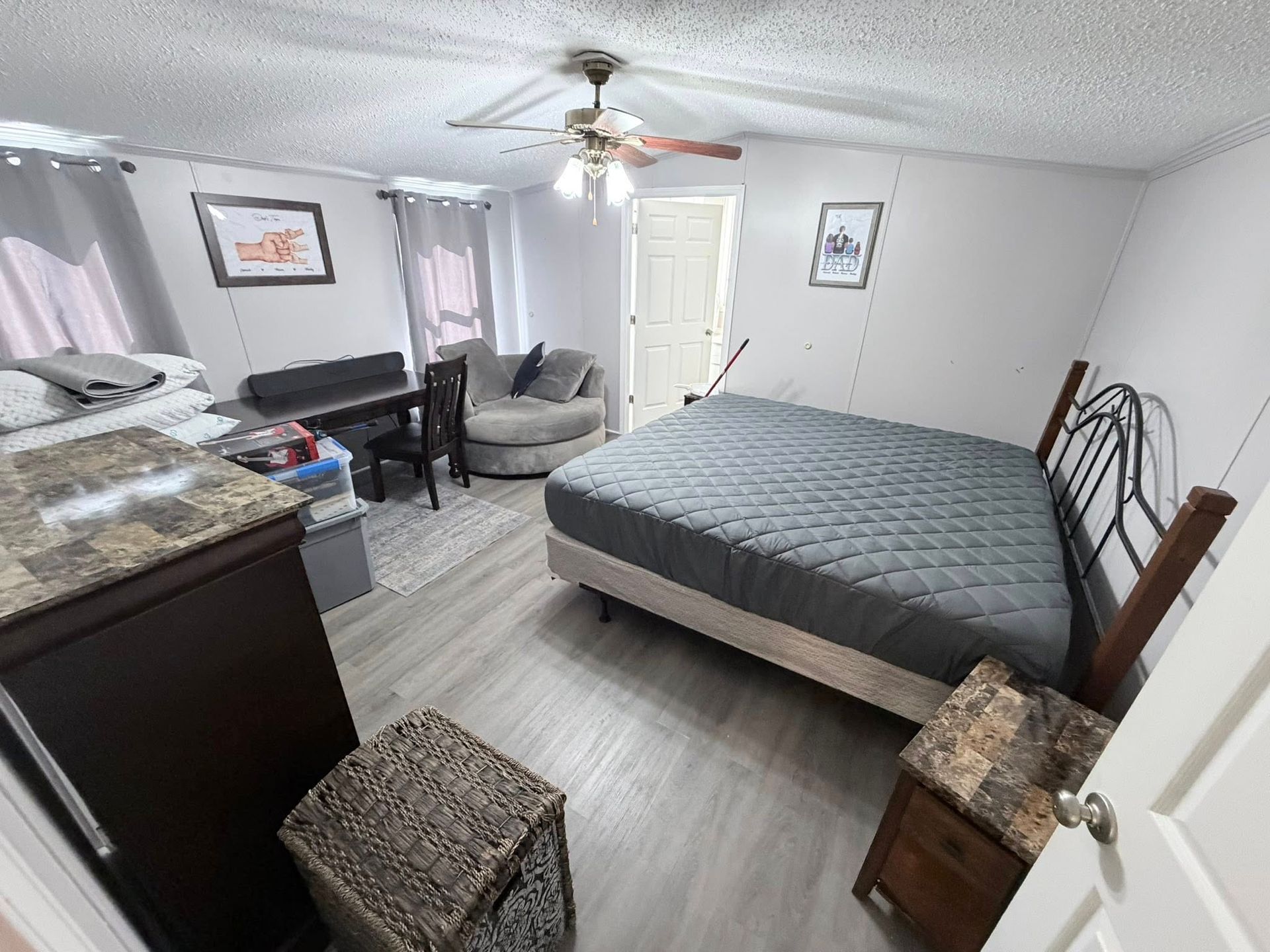 Spare bedroom with a bed, dresser, desk, chair, ceiling fan, and neutral decor.