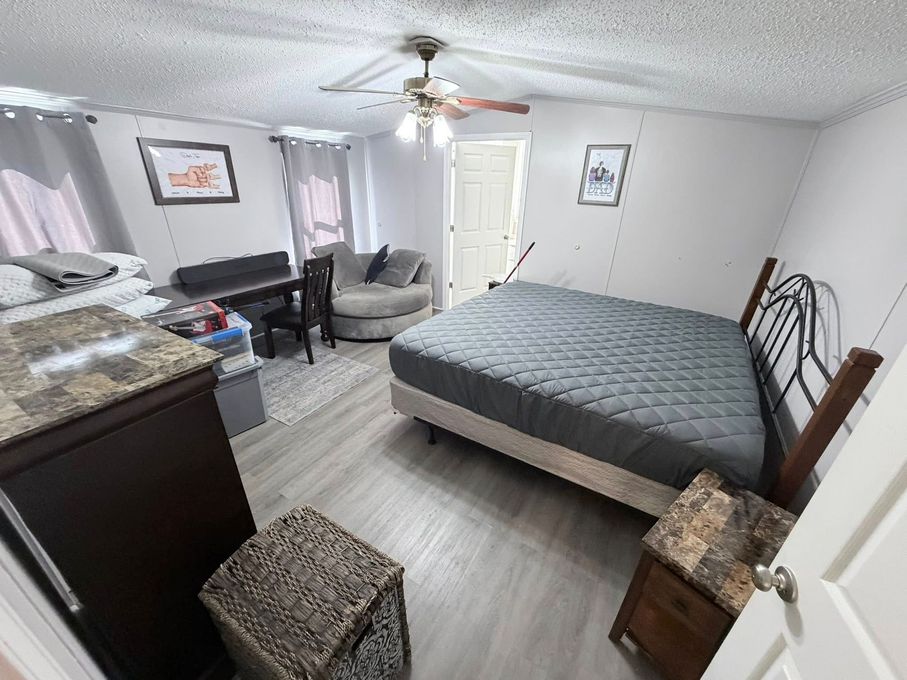 Small bedroom with a bed, desk, chair, dresser, and ceiling fan, in neutral tones.