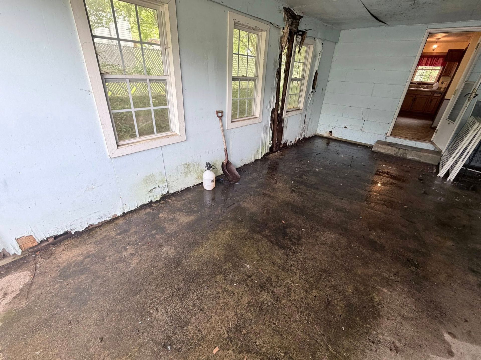 Flood-damaged room with muddy floor, peeling walls, and a window on the left.