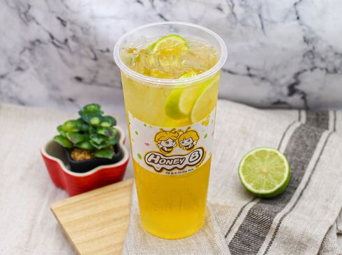 Iced bubble tea in a clear cup on a sunlit table with a logo label and black tapioca pearls