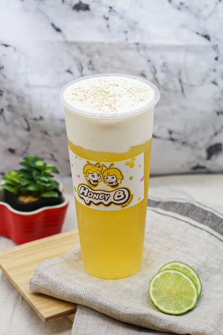 Tall iced yellow drink with foamy top and lime wedge on a table beside a small plant