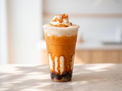 Iced caramel frappuccino topped with whipped cream in a clear cup on a sunlit table