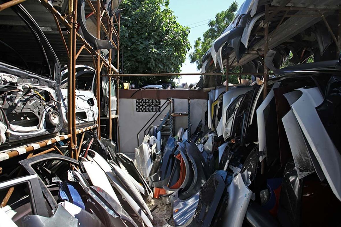 File di pezzi di auto schiacciati e rottami metallici accatastati in un deposito di autodemolizioni all'aperto.