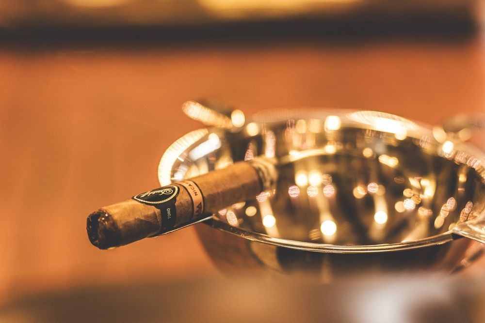 Cigar resting in a silver ashtray, warm, blurred background.