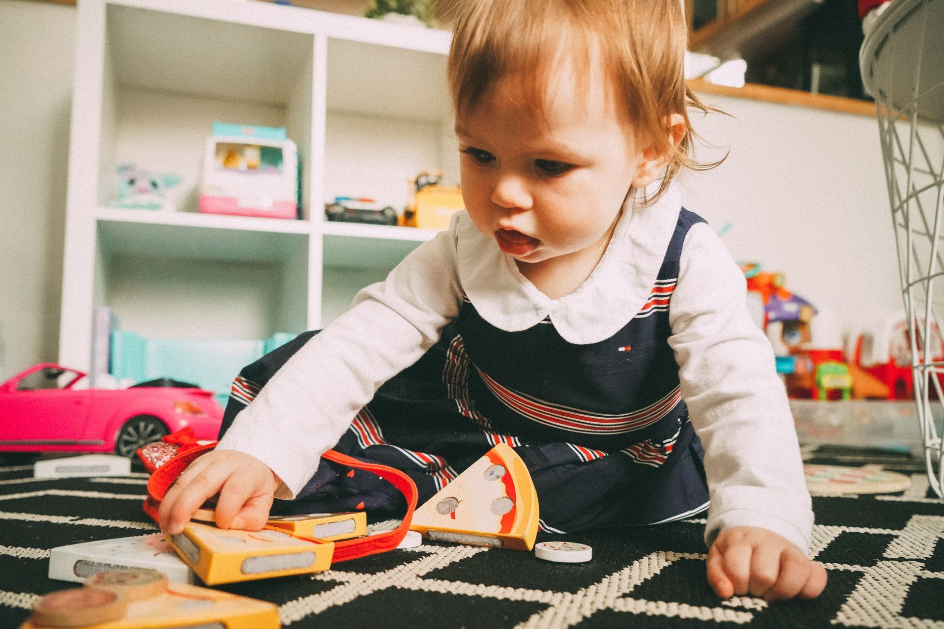 Young child plays with wooden pizza set on carpet in playroom