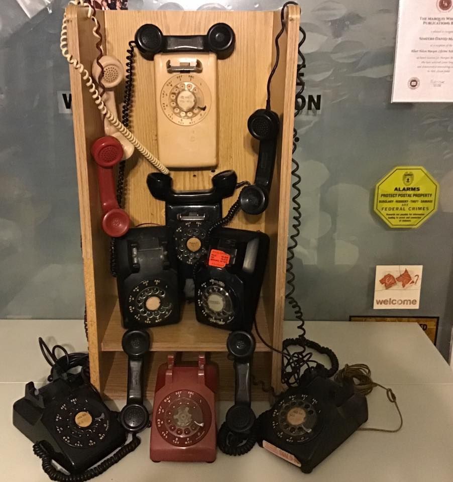 Display of vintage rotary telephones in black, red, and cream on a wall-mounted board.