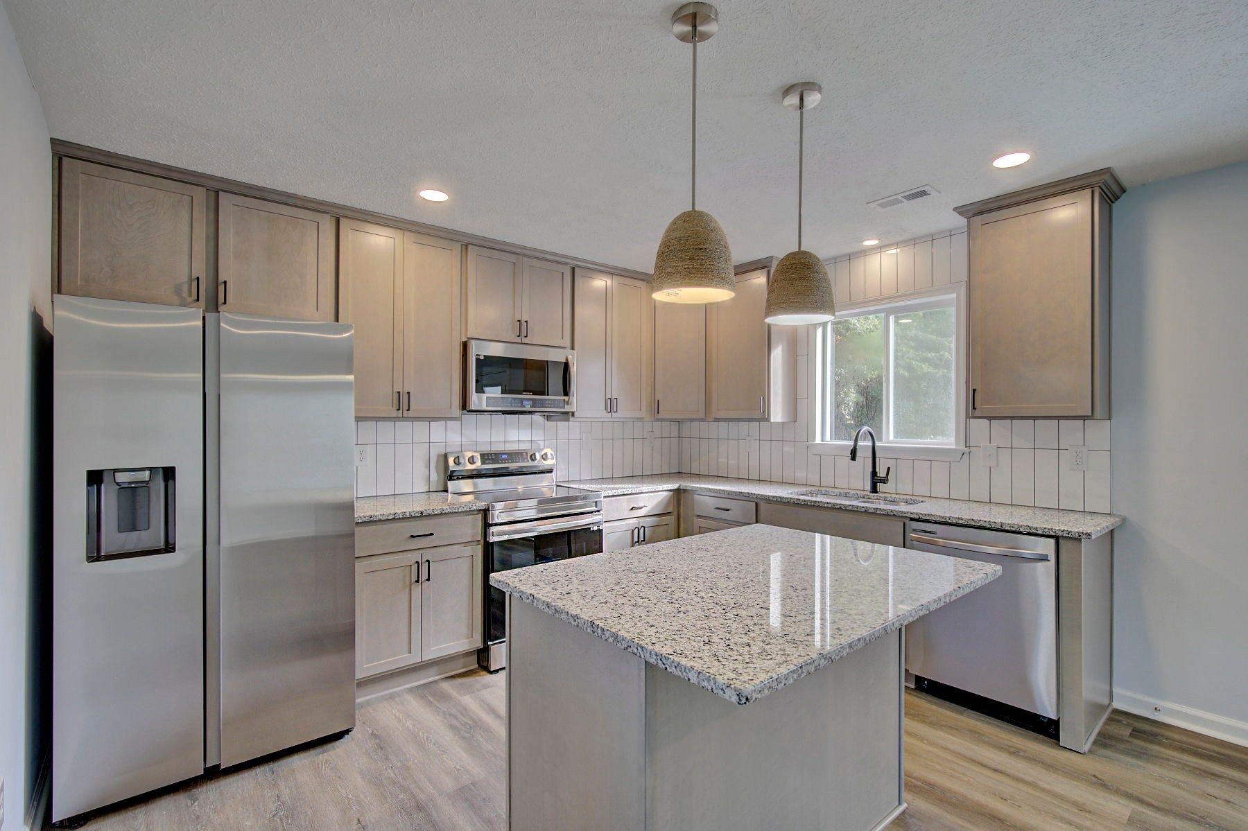 Modern kitchen with stainless steel appliances, white cabinets, and a granite island under pendant lights