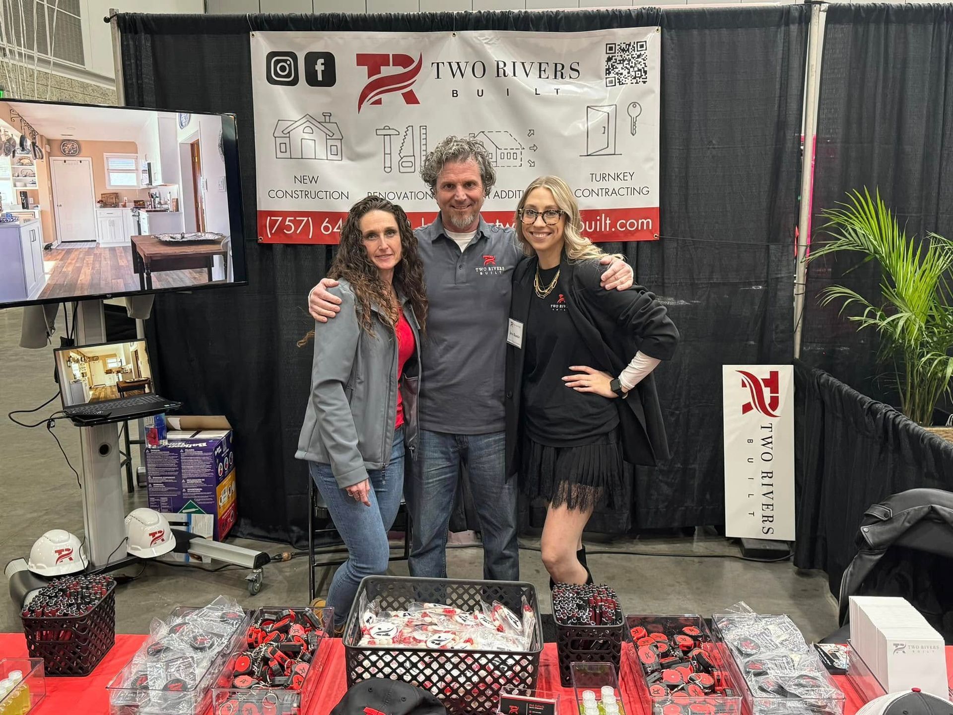 Three people posing at a booth with display tables and banners of assorted products