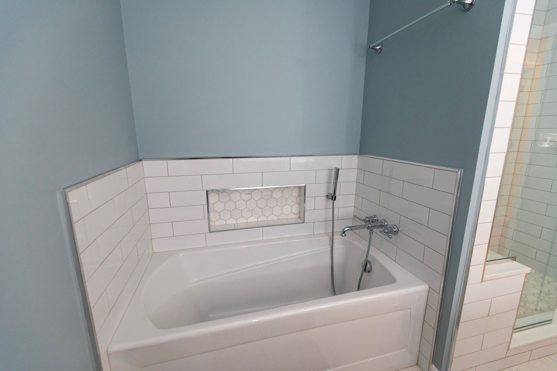Bathroom with a white bathtub, white tile surround, and a wall-mounted shower fixture.