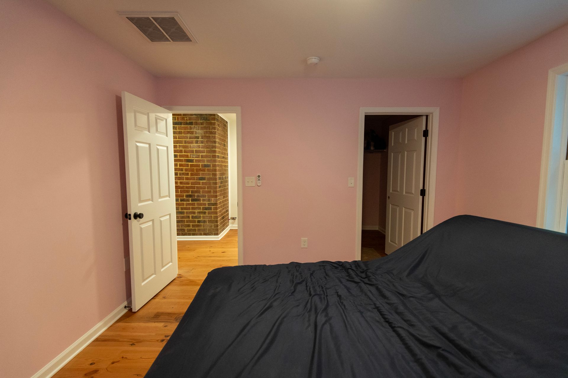 Pink bedroom with black-covered bed, open door to hallway, and dark closet doorway