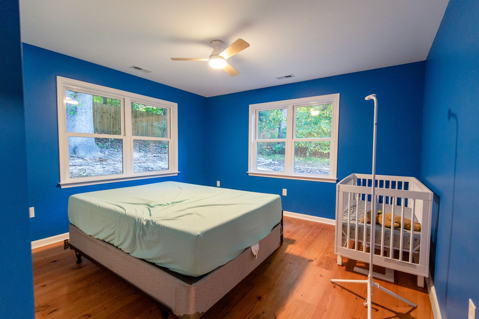 Blue bedroom with bed, crib, and large windows on wood floor
