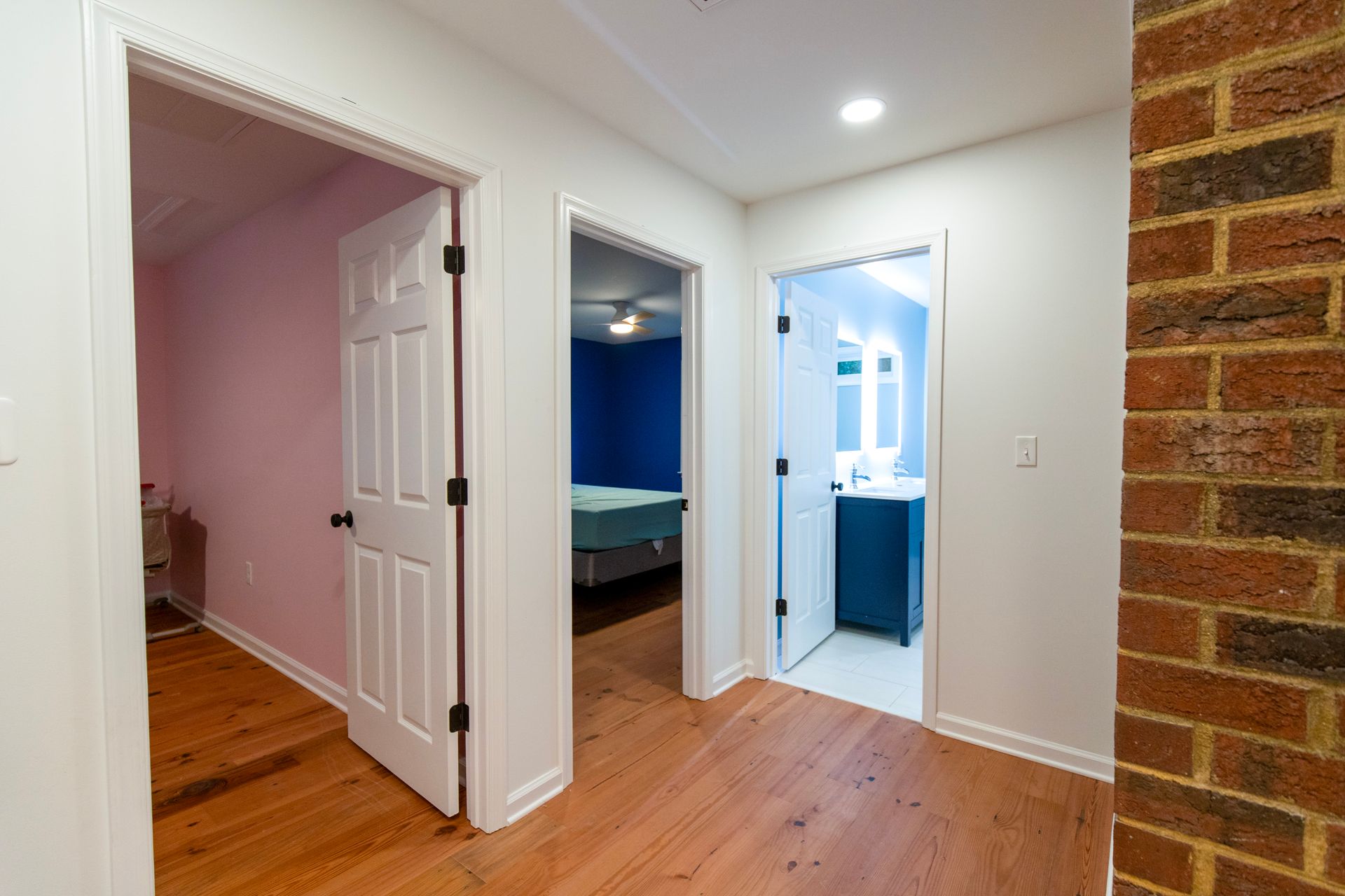 Bright hallway with open doorways, wood floors, blue room, and brick wall accent.