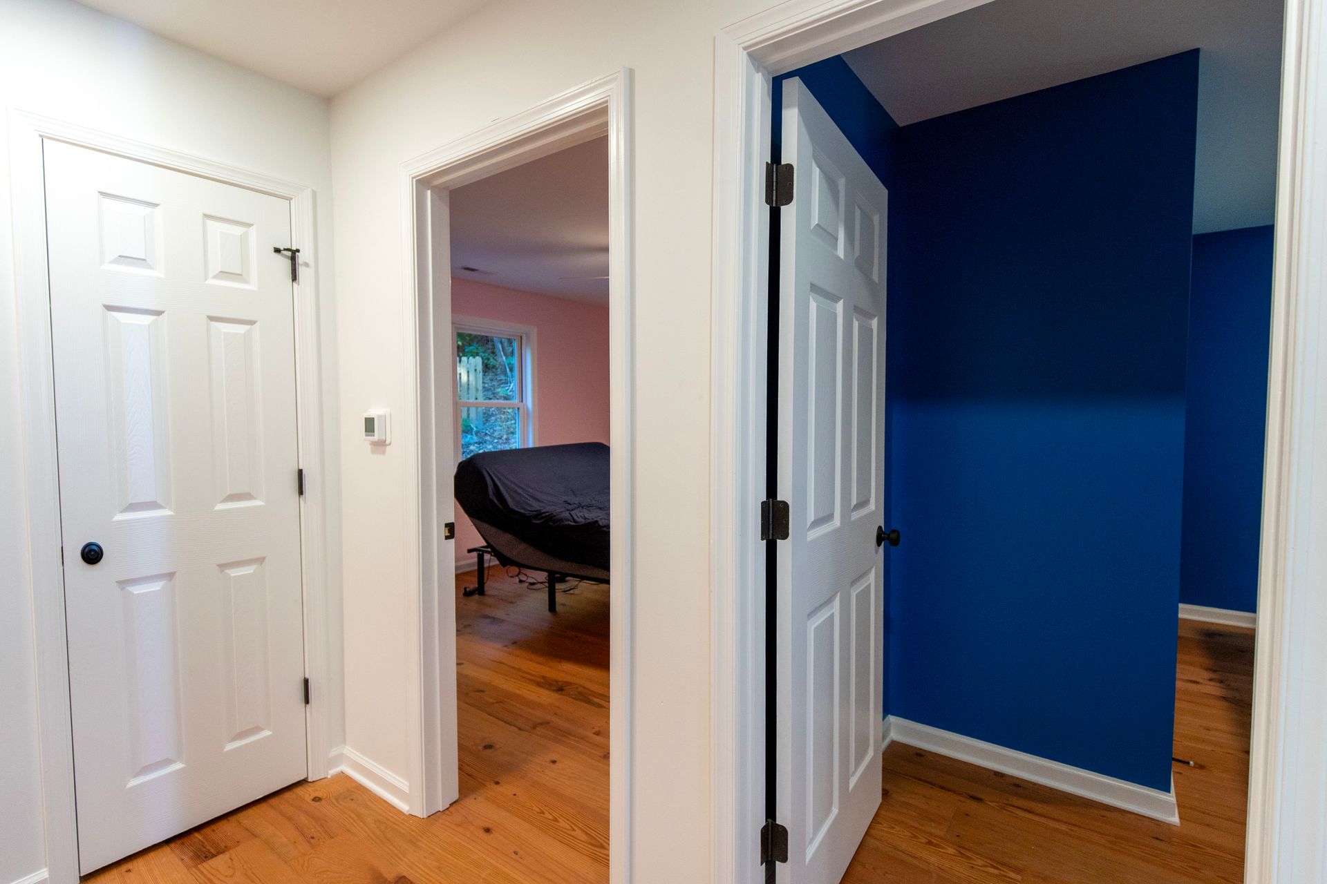 Bright hallway with white doors, hardwood floors, and a blue-walled room visible through an open doorway.