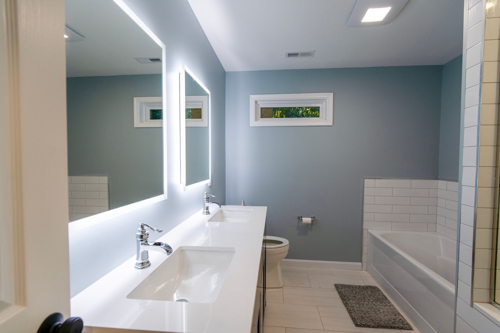 Modern bathroom with double vanity, large mirror, and glass-enclosed tub shower in light blue and white.