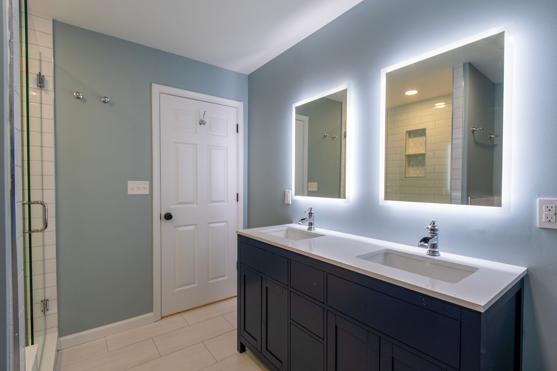 Modern bathroom with double vanity, illuminated mirrors, and light blue walls