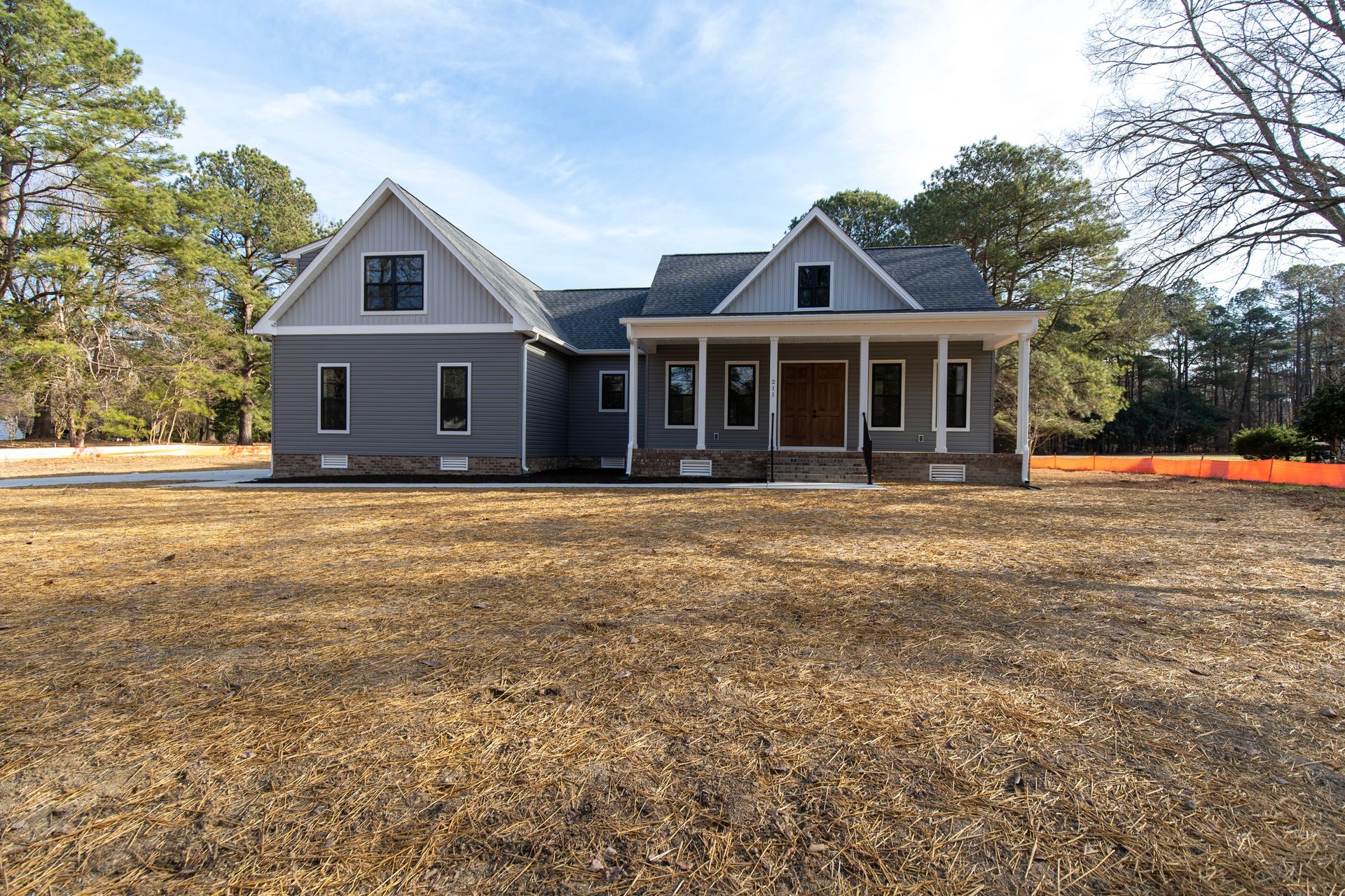 Gray farmhouse with a front porch and large yard under a blue sky