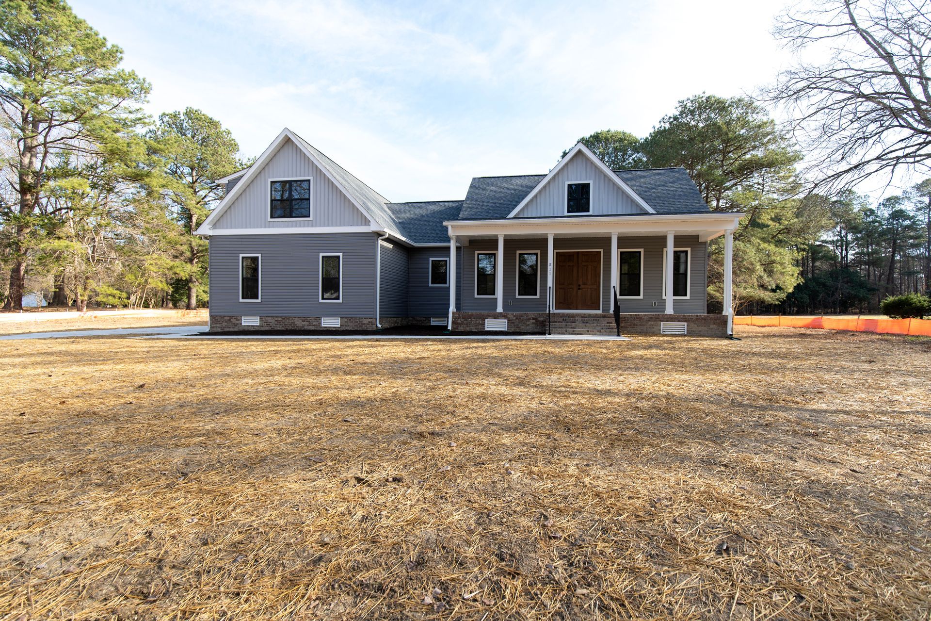 Gray farmhouse with a covered front porch on a large, leaf-covered yard under clear skies