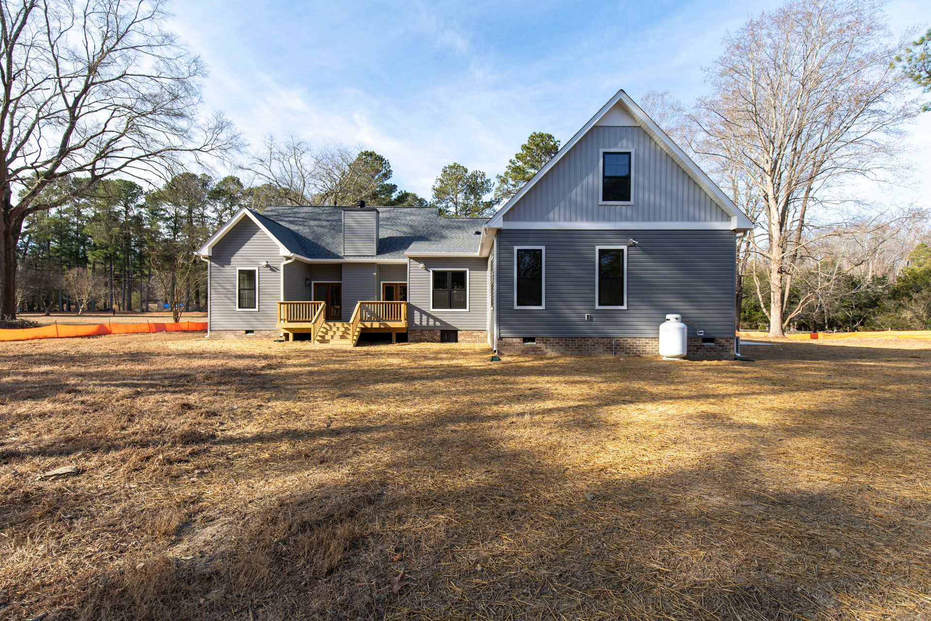 Gray farmhouse with porch and large yard under a clear sky