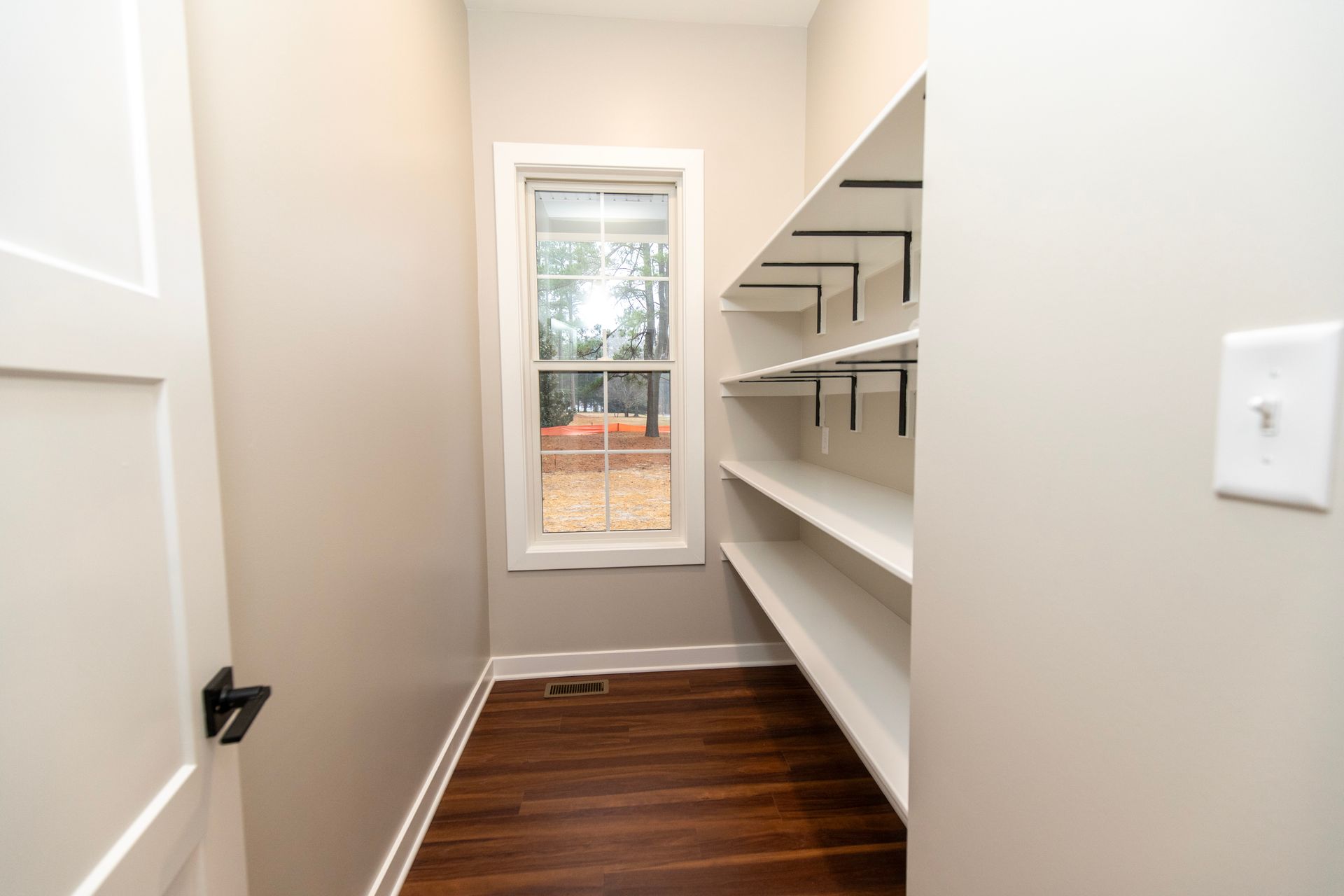 Walk-in closet with white shelves, dark wood floor, and a window at the end.