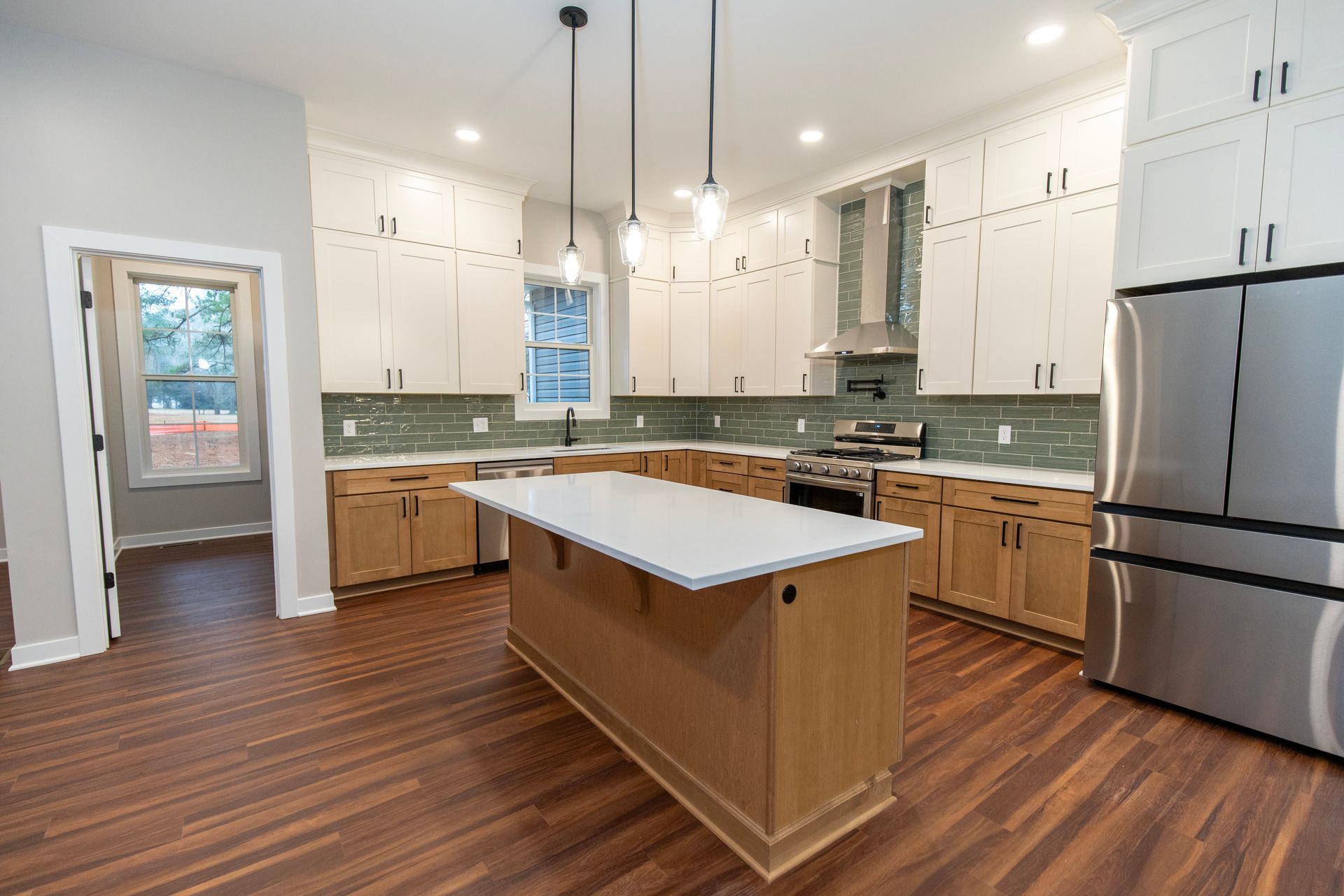 Modern kitchen with white cabinets, wood floors, island, and stainless steel refrigerator