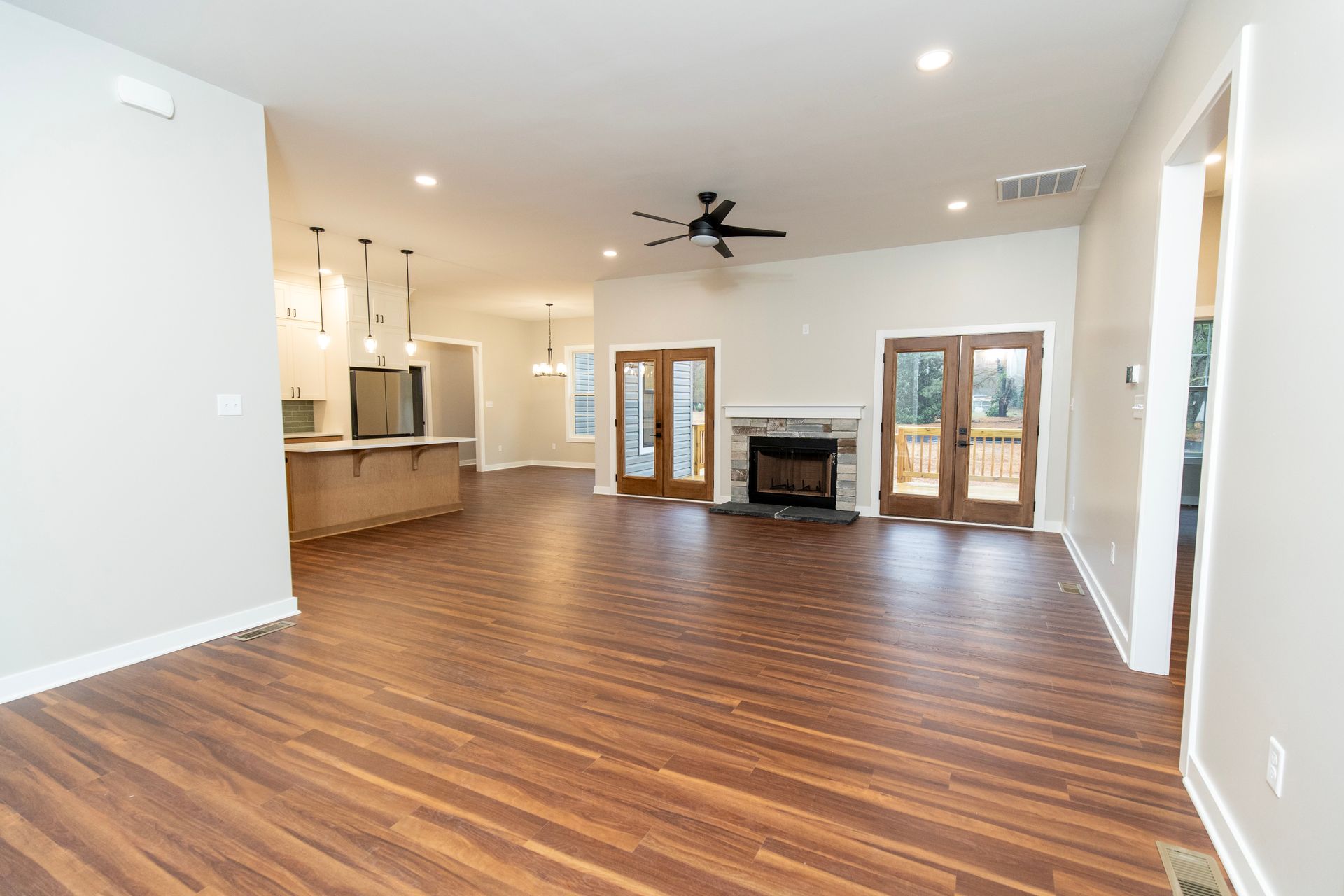 Spacious open-concept living room with wood floors, fireplace, ceiling fan, and kitchen area in the background