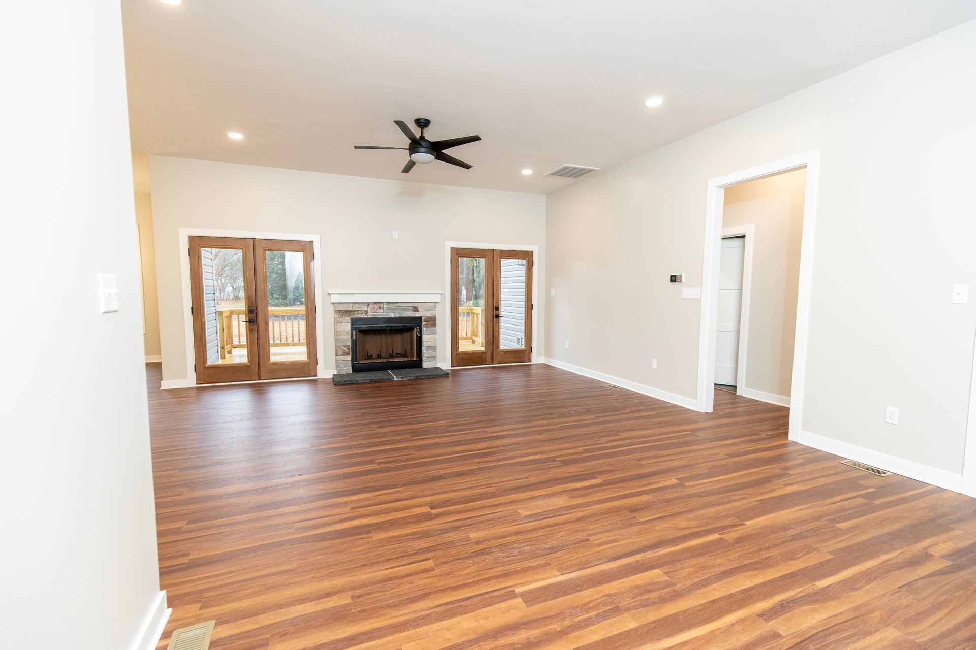 Spacious empty living room with wood floors, fireplace, ceiling fan, and French doors.