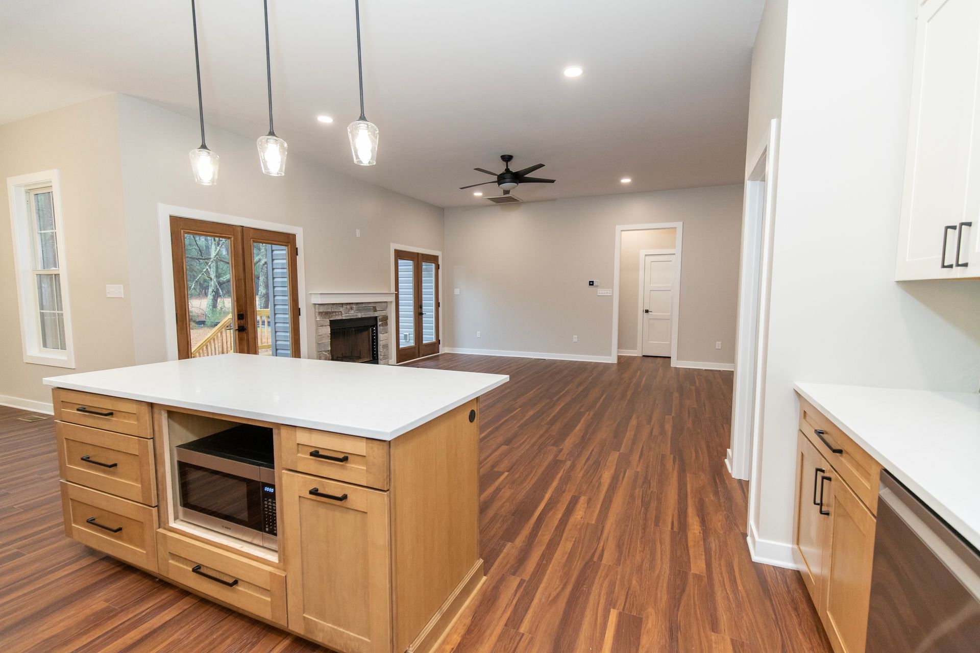 Modern open kitchen with white cabinets, island, wood floors, and ceiling fan leading into a living area