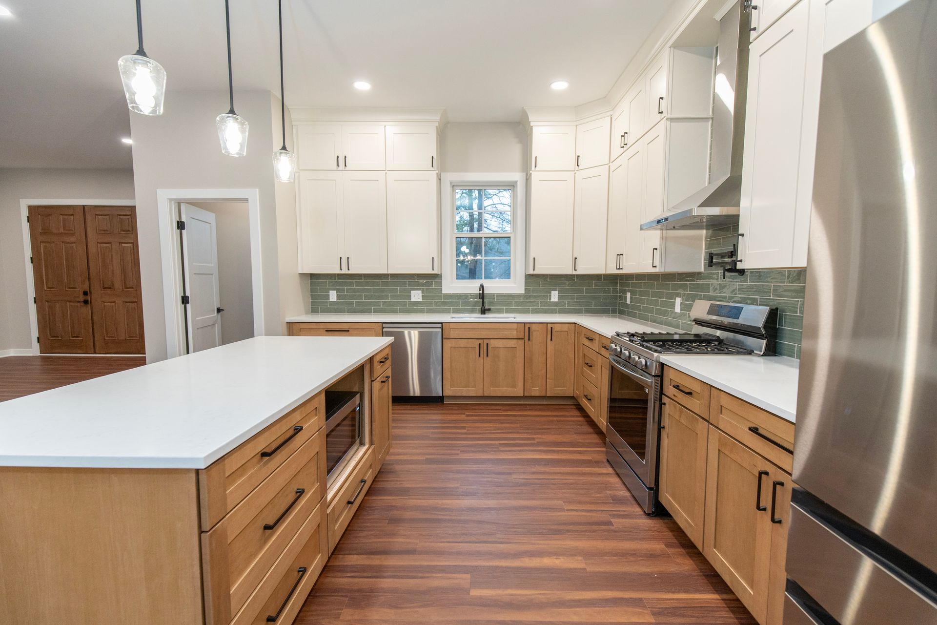 Bright modern kitchen with white cabinets, wood floors, island, and stainless steel appliances