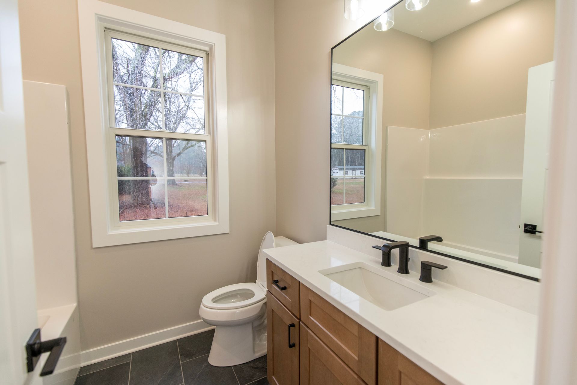 Modern bathroom with white vanity, large mirror, window, and toilet beside the sink.