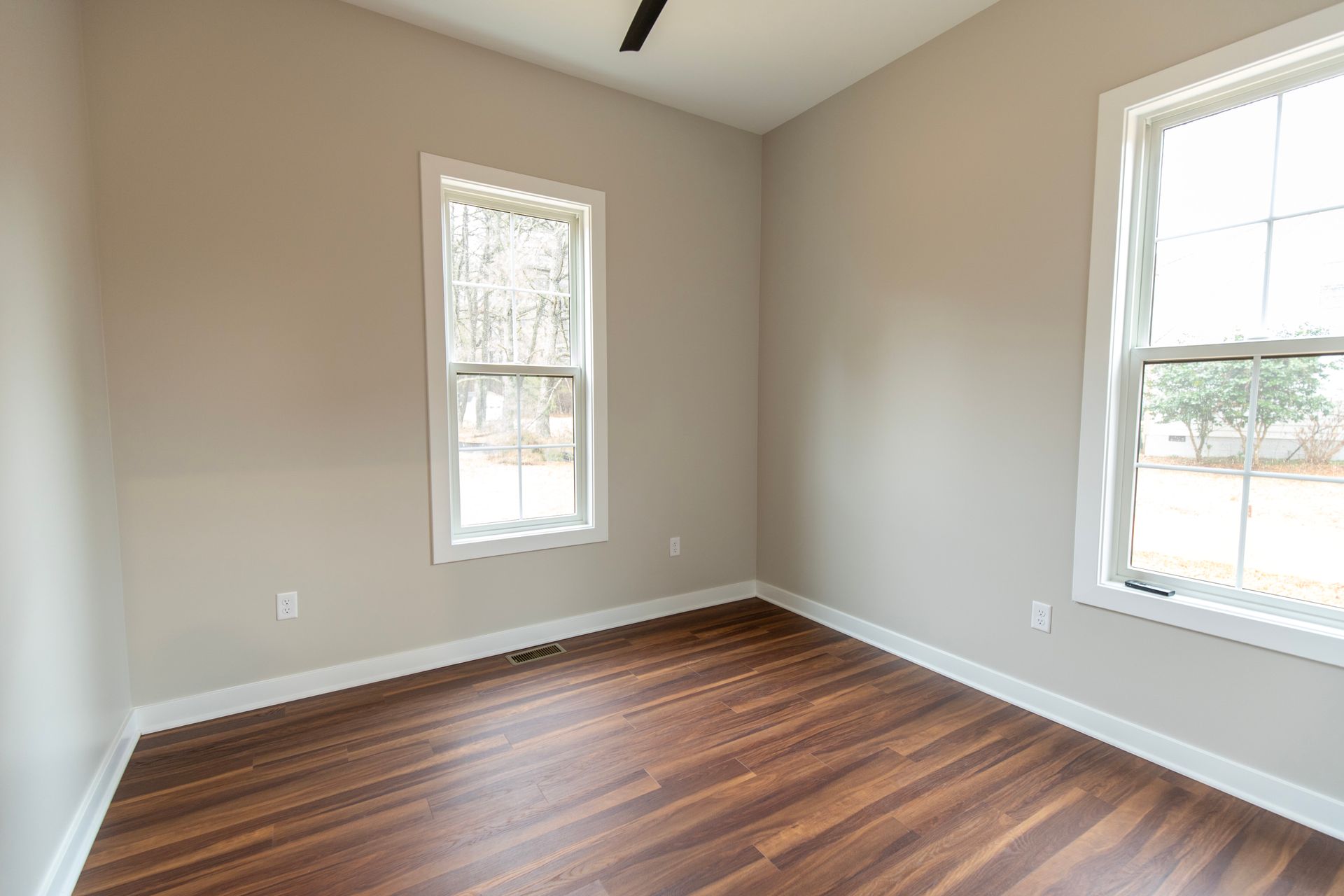 Empty beige room with two windows and dark wood floors
