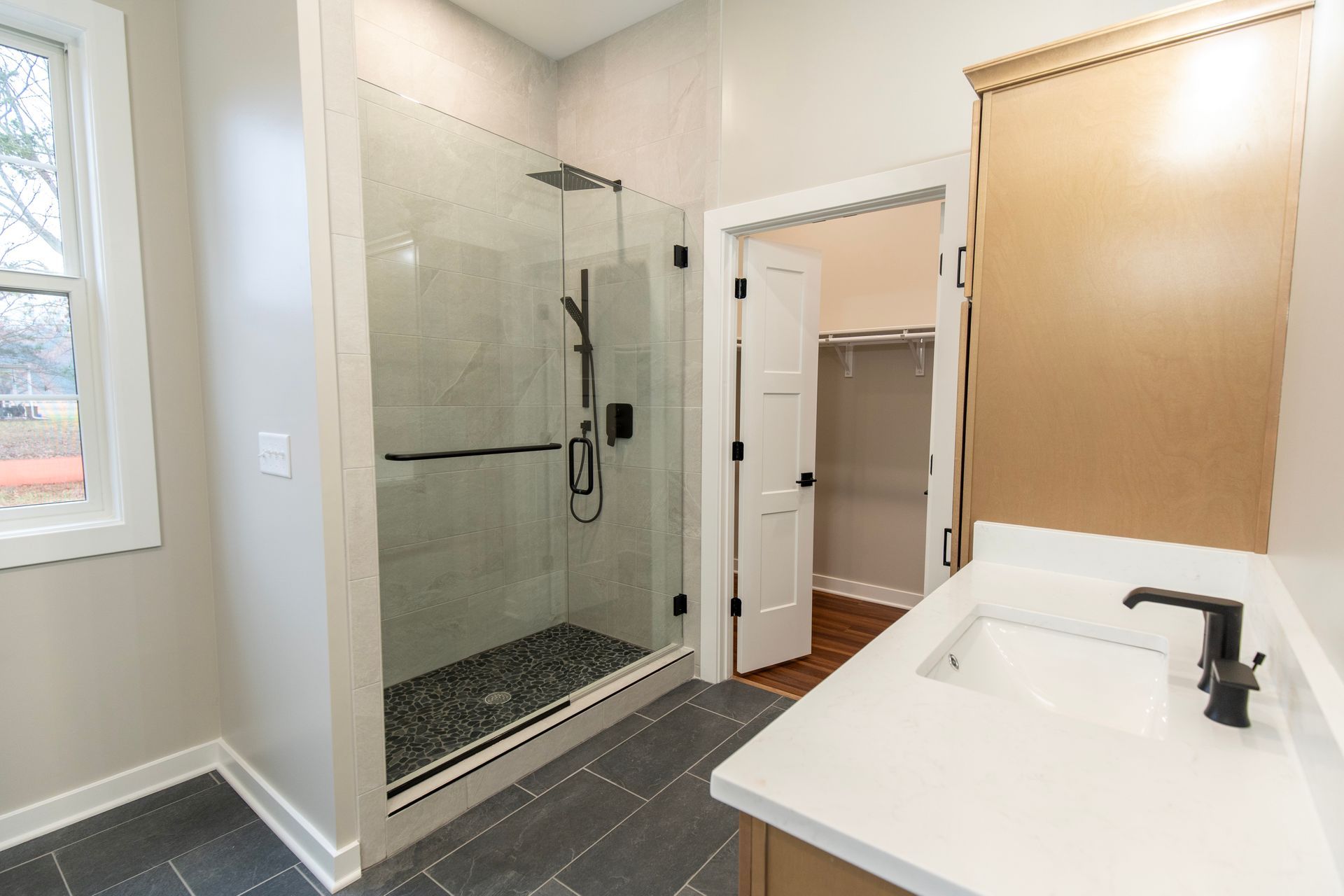 Accessible bathroom with walk-in glass shower, white vanity, and open linen closet.