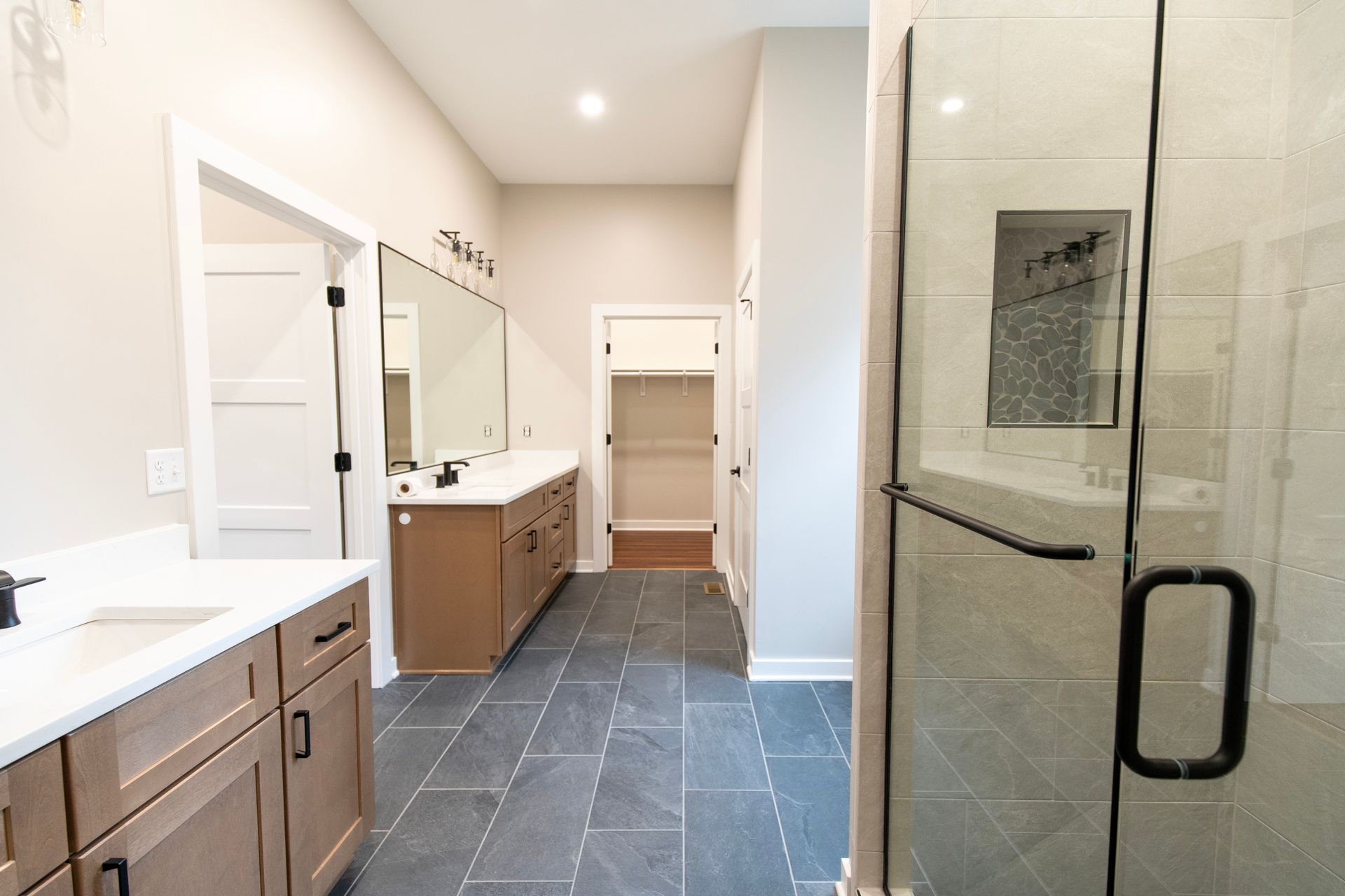 Modern bathroom with double vanity, large mirror, and glass shower door on slate tile floor